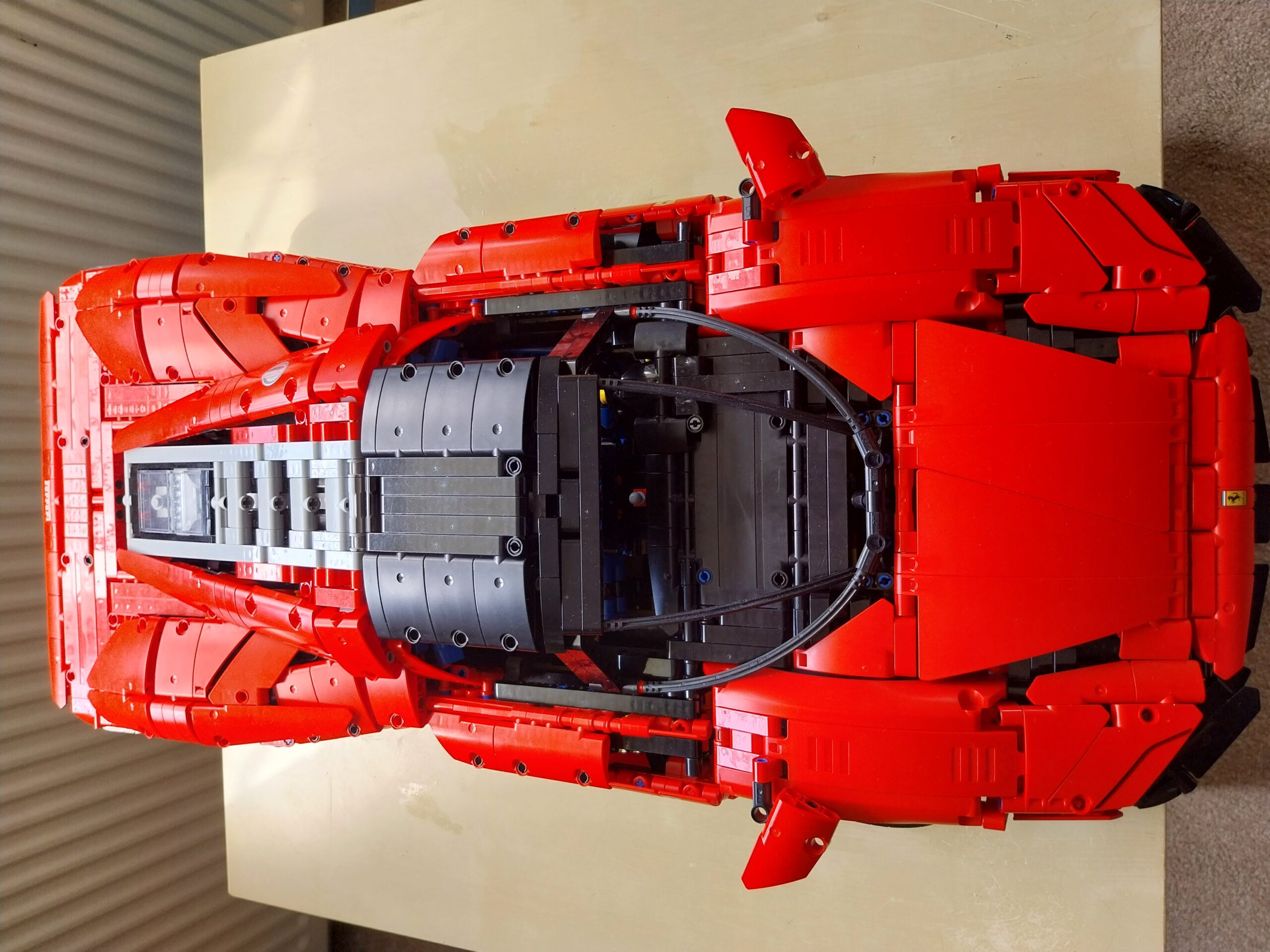 Completed LEGO Technic Ferrari Daytona SP3 42143 build, front three-quarter view showing red body panels and butterfly door open