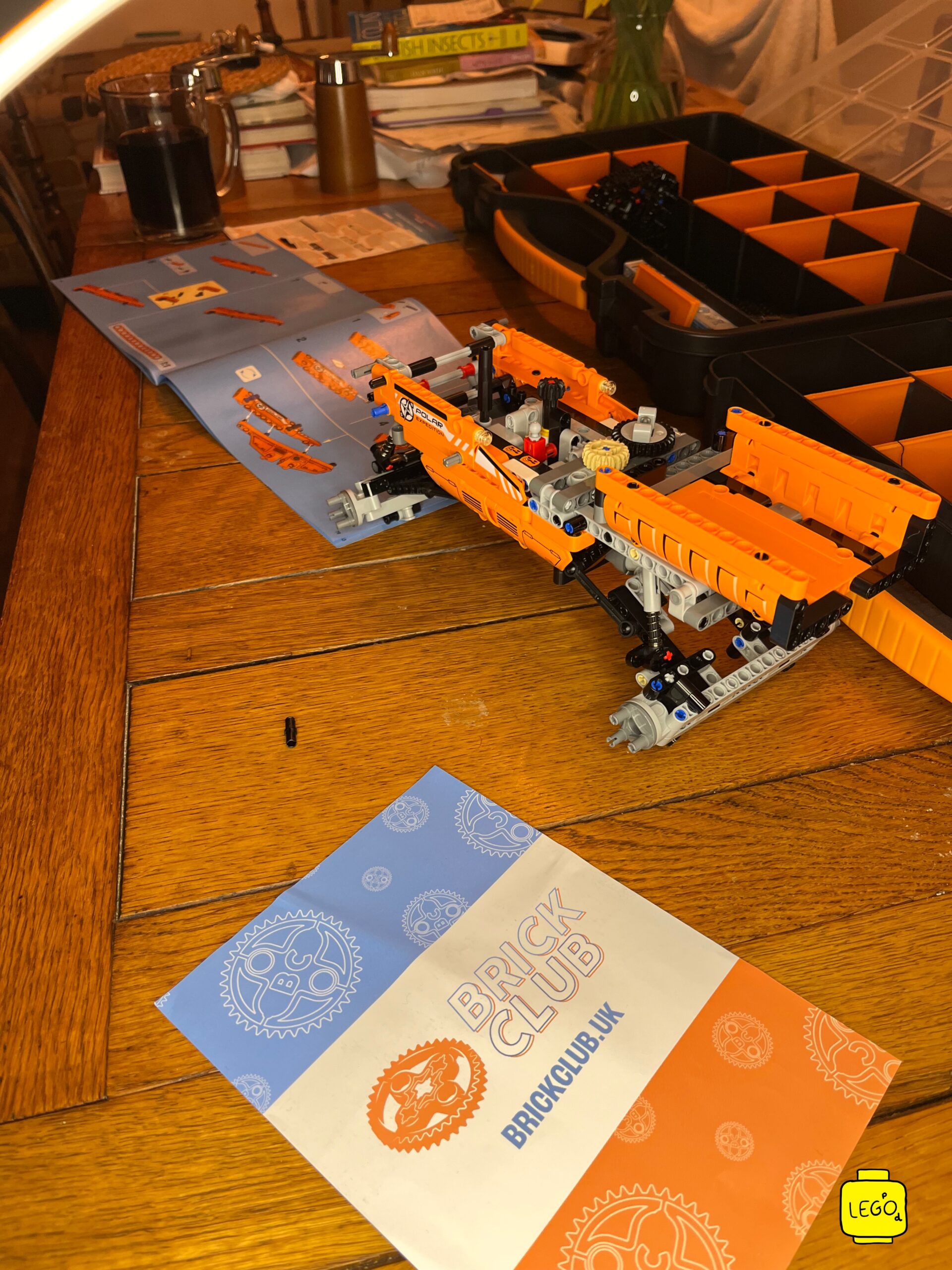LEGO Technic 42099 X-treme Off-Roader mid-build with instruction manual and Brick Club delivery card on wooden table
