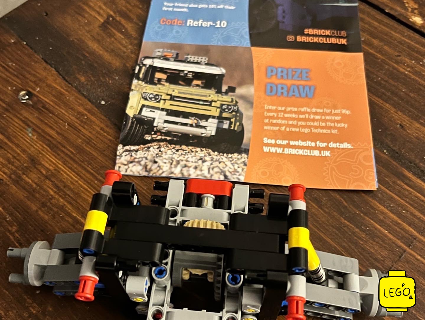 LEGO Technic 42111 Doms Dodge Charger chassis assembly on wooden table with Brick Club prize draw card visible