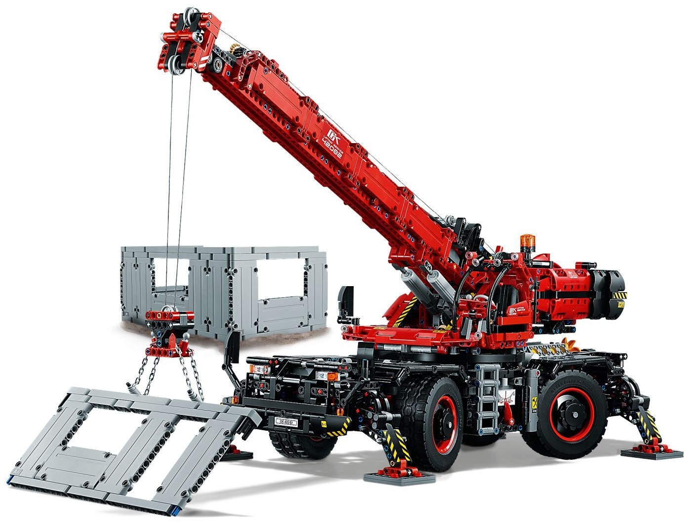LEGO Technic Rough Terrain Crane (42082) with all four outriggers down on pads, boom raised and lifting a grey wall section, with the other wall sections assembled behind