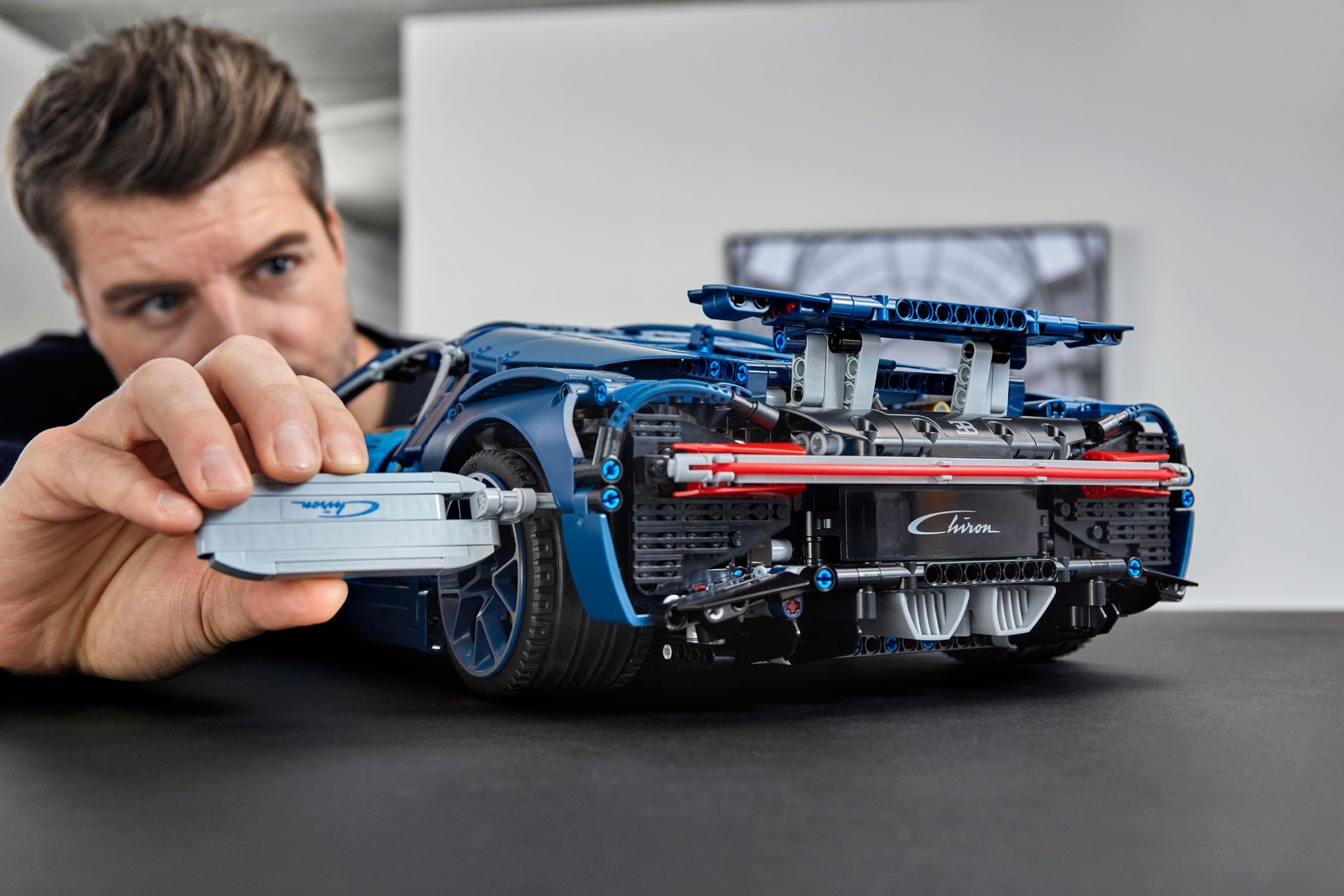 A builder pushing the grey speed key into the port behind the rear wheel of LEGO Technic Bugatti Chiron (42083), rear wing raised, red light bar across the back