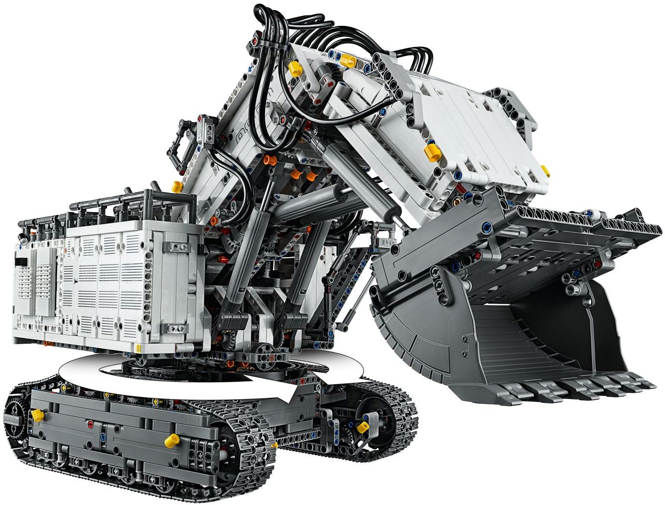 Rear three-quarter view of LEGO Technic Liebherr R 9800 Excavator (42100) showing the white superstructure on its turntable above the dark grey tracks, the grey linear actuators under the boom, and the bucket raised on the right