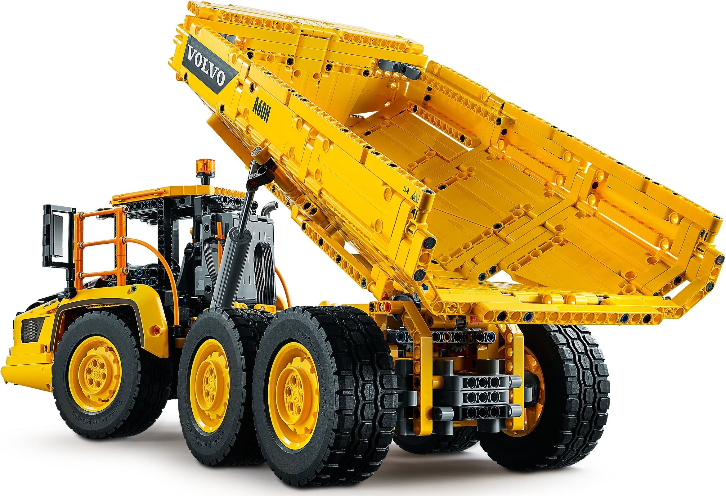 Rear three-quarter view of LEGO Technic 6x6 Volvo Articulated Hauler (42114) with the yellow bed tipped up, showing one of the grey linear actuators, the exposed gearing under the bed and the hub behind the cab