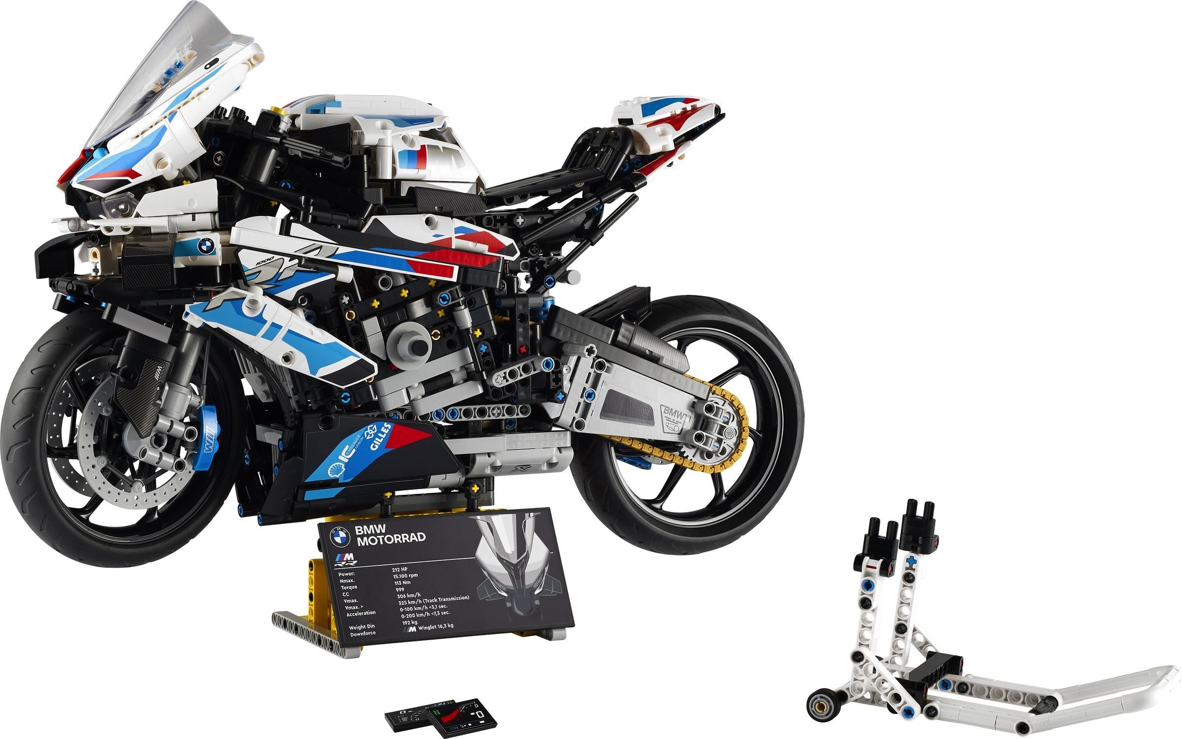 LEGO Technic BMW M 1000 RR (42130) on its display plate with the BMW Motorrad specification plaque, the separate racing stand and two spare dashboard tiles laid out beside it, official product image