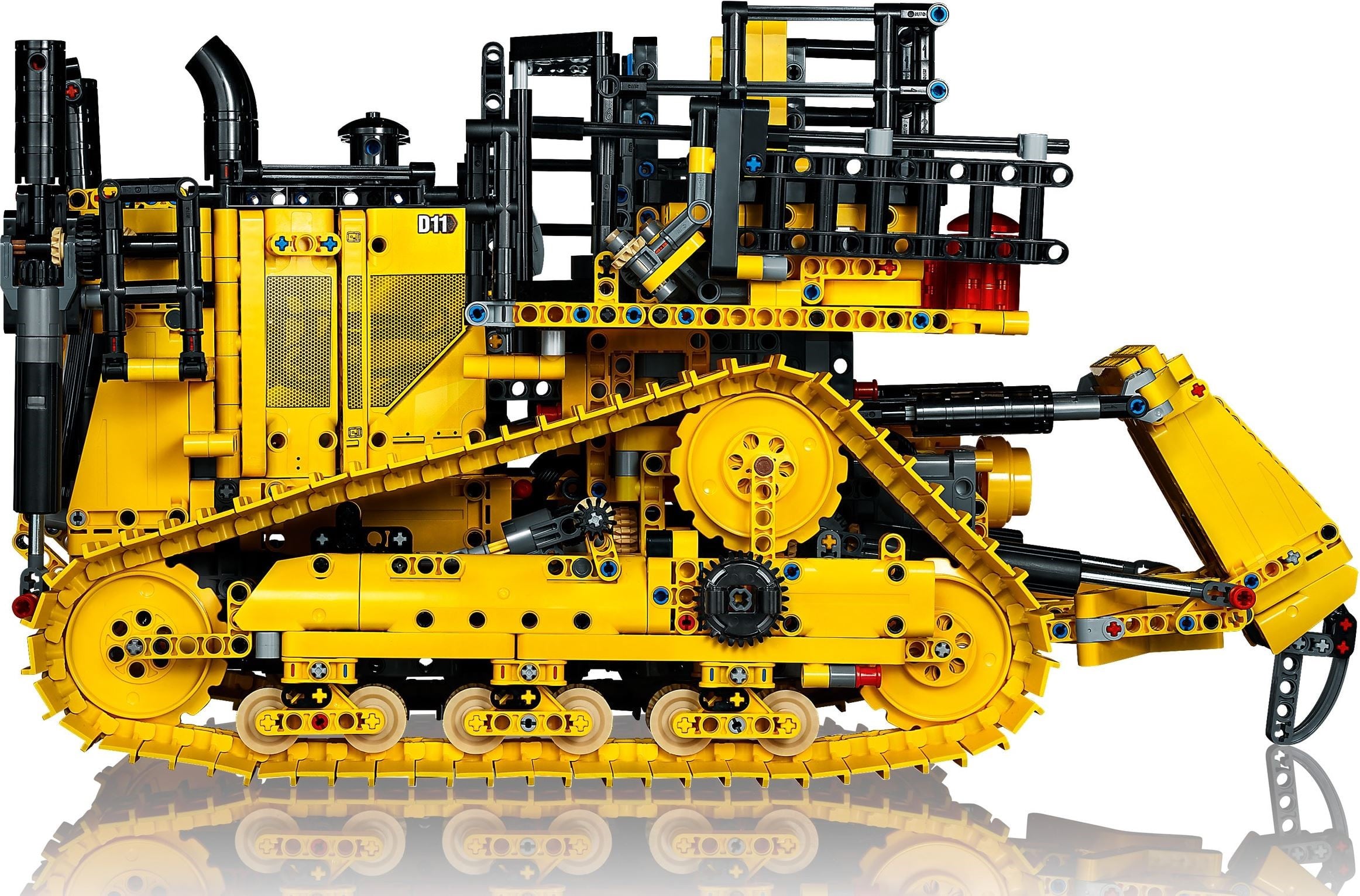 Side view of LEGO Technic Cat D11 Bulldozer (42131) showing the wide yellow tracks, the raised yellow drive sprocket with a black gear on the track frame below it, the ripper on the right, the mesh grille panels, the exhaust stack and the roll cage over the cab
